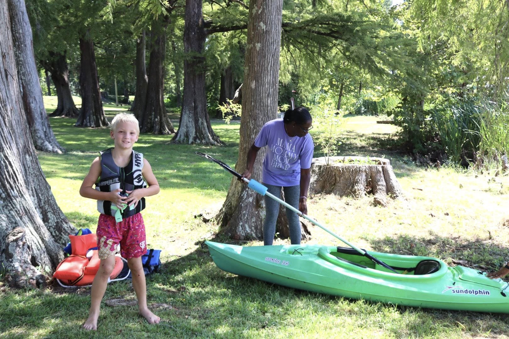 A boy putting on a lifejacket and a woman looking at a kayak.